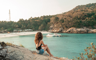 Happy woman sitting at the beach on a sunny day. Sexy perfect fit body woman. Portrait of glamour lady enjoying her vacation on beach shore. Back view