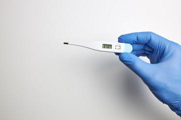 Hand with latex glove holding digital thermometer marking high temperature.