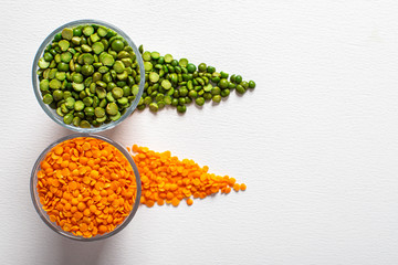 two types of legumes, beautifully arranged in cups and on a white background - green peas and orange lentils. Top view. copy space. Vegetarian food.