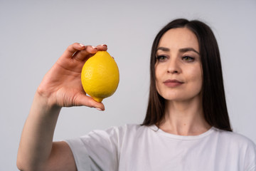 Beautiful girl holding a lemon at eye level and looks at it, the concept of beauty and health