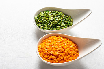 two types of legumes, beautifully arranged in cups and on a white background - green peas and orange lentils. Top view. copy space. Vegetarian food.