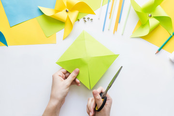 How to make paper green windmill toy with children at home. Step by step instructions. Hands making DIY summer project. Step 5. Cut sheet in lines to circle in center, getting half-cut triangles.