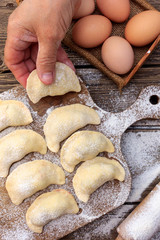 raw dough dumplings lie in row on wooden board on brown table with flour