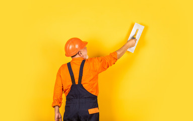 Plasterer in working uniform plastering wall indoor. man with spatula. process of applying layer of...