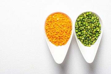 two types of legumes, beautifully arranged in cups and on a white background - green peas and orange lentils. Top view. copy space. Vegetarian food.