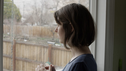 Woman walks up to window and looks outside with a blank look on her face.