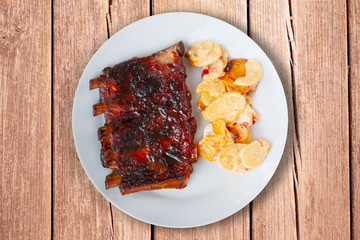 Spicy hot grilled spare ribs from BBQ served on a plate with paprika scalloped potatoes on rustic wood table. Close-up flat top view image.