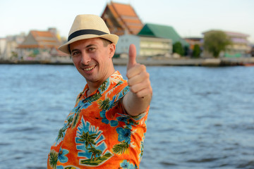 Fototapeta premium Happy young handsome tourist man at pier against view of the river