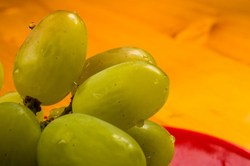 large brush of green grapes in a red ceramic plate on a wooden background