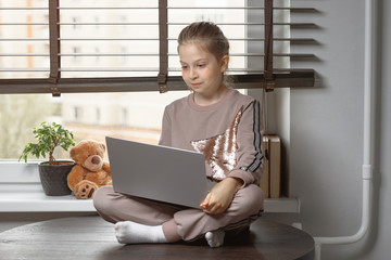 Cool online school. A child learns online at home using a laptop. Cheerful little girl using laptop...
