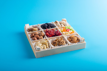 Assorted dried fruits and nuts in a wooden box isolated on a blue background. Raisins, candied fruits, cherries, Brazil nuts, hazelnuts, walnuts, almonds, cashews, pistachios.