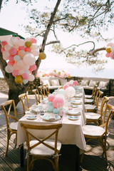 Wedding dinner table reception. A rectangular table in the style of rustic with a cream tablecloth and handmade wooden chairs. A table in the shade of trees, outside, decorated with lots of balloons
