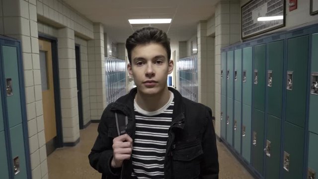 High school boy student walking along lockers in corridor