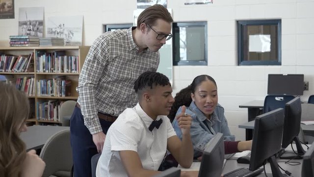 High school teacher helping students at computers in library
