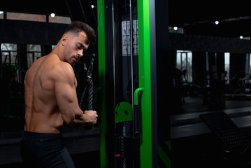 Fototapeta na wymiar male athlete shows near the green simulator how to perform the exercise for the deltoid and biceps and triceps muscles in the gym, sexy guy bodybuilder, sports lifestyle, home sports.