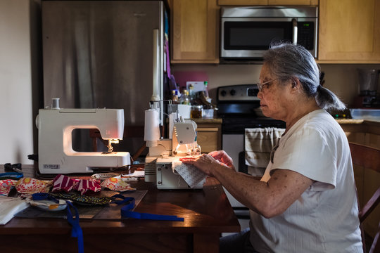 Side view of senior woman sewing masks from fabric at home