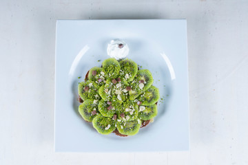 Tart with kiwi and whipped cream and 
pistachio on white table. Fresh green kiwi pie