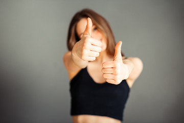 Girl in a black top with her hair shows thumb up. On a gray background. Without makeup, without retouching.