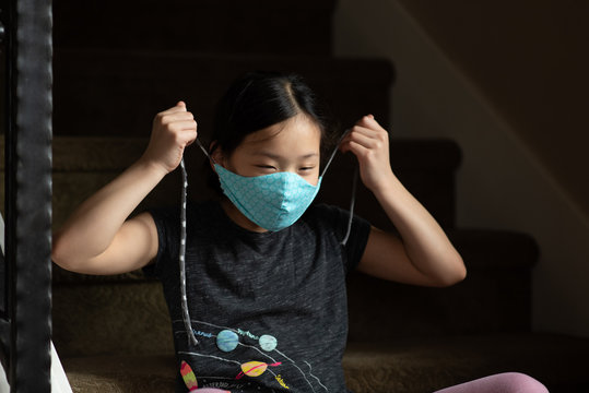 Asian girl pulls strings of cloth face mask around head