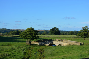 Summer landscape with old stone bridge over Hovingham Beck,  North Yorkshire, England