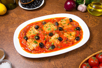 Pan seared fish with tomatoes and olives on an brown table. Selected focus.