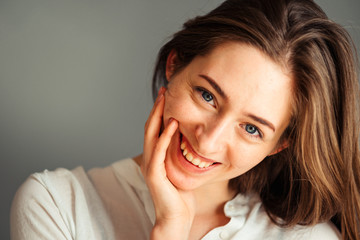 Close-up portrait of a smiling young girl in a white shirt on a gray background. in a good mood. Without retouching and makeup.