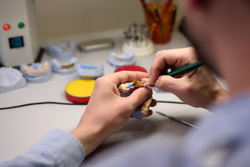 Close-up of a dental technician holding a tooth model in his hands and working to create dentures in a laboratory.