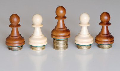 Five pawns of chess pieces on columns of coins symbolizing the exclusion from equal income