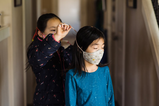 Sister helps girl tie on cloth face mask at home