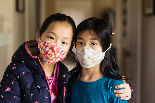 Two Asian sisters at home wearing cloth masks