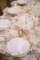 Wedding dinner table reception. Delicate creamy pastel tones of tablecloths and plates on table, three forks left and two knives on right, glasses and candles in candlesticks
