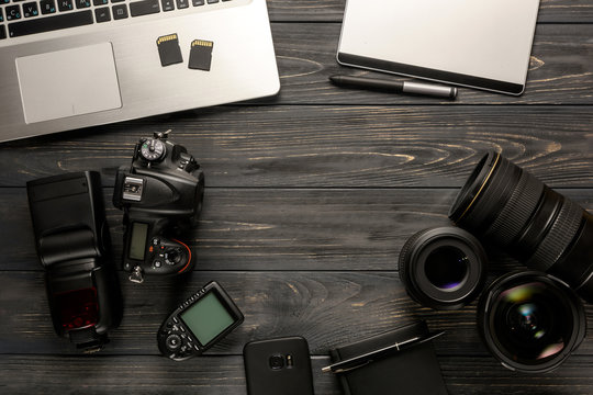 Top view on freelancer photographer workspace. DSLR camera, laptop, flash, wireless trigger, graphics tablet and photo accessories on a dark wooden table.
