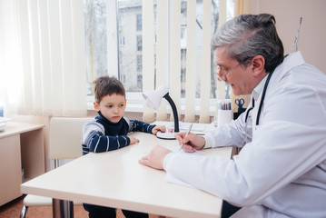 Fototapeta premium A young boy is listened to and treated by an experienced doctor in a modern clinic. A virus, and an epidemic