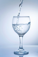 Water pouring into  wine glass on a white background, close up