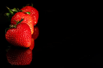 Three ripe strawberries on a black background with a reflection with a copy space