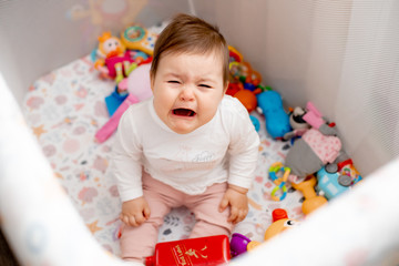 Baby girl sits among toys, cries