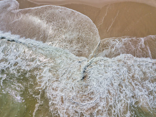 Aerial drone image of foamy waves washing up on the beautiful sandy beach of Island Beach State Park in New Jersey creating colorful abstract images