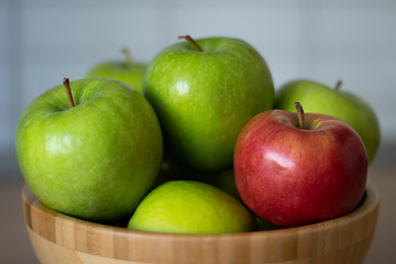 Wooden bowl with green apples and one red Apple close - up in the center of the frame