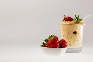 Fresh strawberries in a white saucer and tiramisu in a glass glass on a white background
