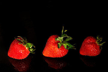 Three fresh strawberries on a black background with a reflection