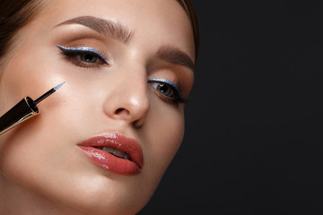 Beautiful girl with sexy lips and classic makeup with cosmetic blue eyeliner in hand. Beauty face. - obrazy, fototapety, plakaty