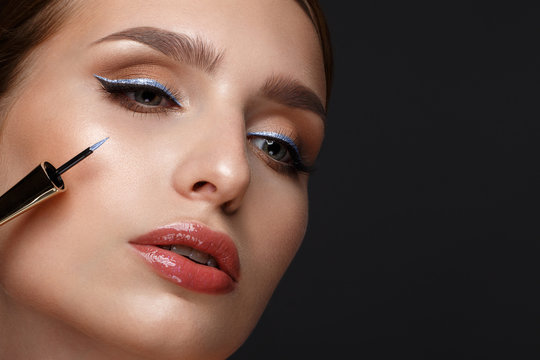 Beautiful girl with sexy lips and classic makeup with cosmetic blue eyeliner in hand. Beauty face.