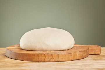 Fototapeta na wymiar Raw wheat dough on wooden cutting board. Close up
