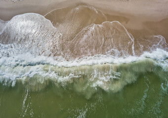 Aerial drone image of foamy waves washing up on the beautiful sandy beach of Island Beach State Park in New Jersey creating colorful abstract images