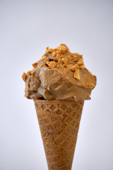 Peanut butter banana ice cream cone with sprinkles of peanuts on top on a white background - gluten-free waffle cone 