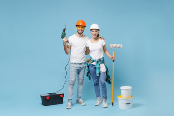 Funny couple woman man in helmet hardhat glasses hold paint bucket paint roller, electric drill...