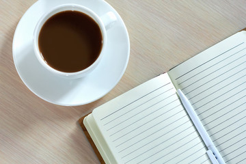 Top view of a white coffee Cup with a notebook and pen on the table. The concept of business planning and organization during a break and Breakfast