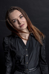 A makeup brunette girl in a black dress is standing and looking at the viewer. Studio portrait on a dark background. Vertical orientation.