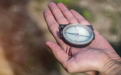 Male holding a military compass in outstretched hand. Man holding an old compass on the palm of the hand showing direction. Outdoor photo, close up, blurred background.	