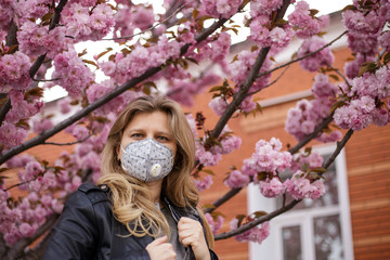 Girl in a mask a respirator. Quarantine isolation during a coronavirus pandemic. Portrait against the background of a blossoming sakura tree